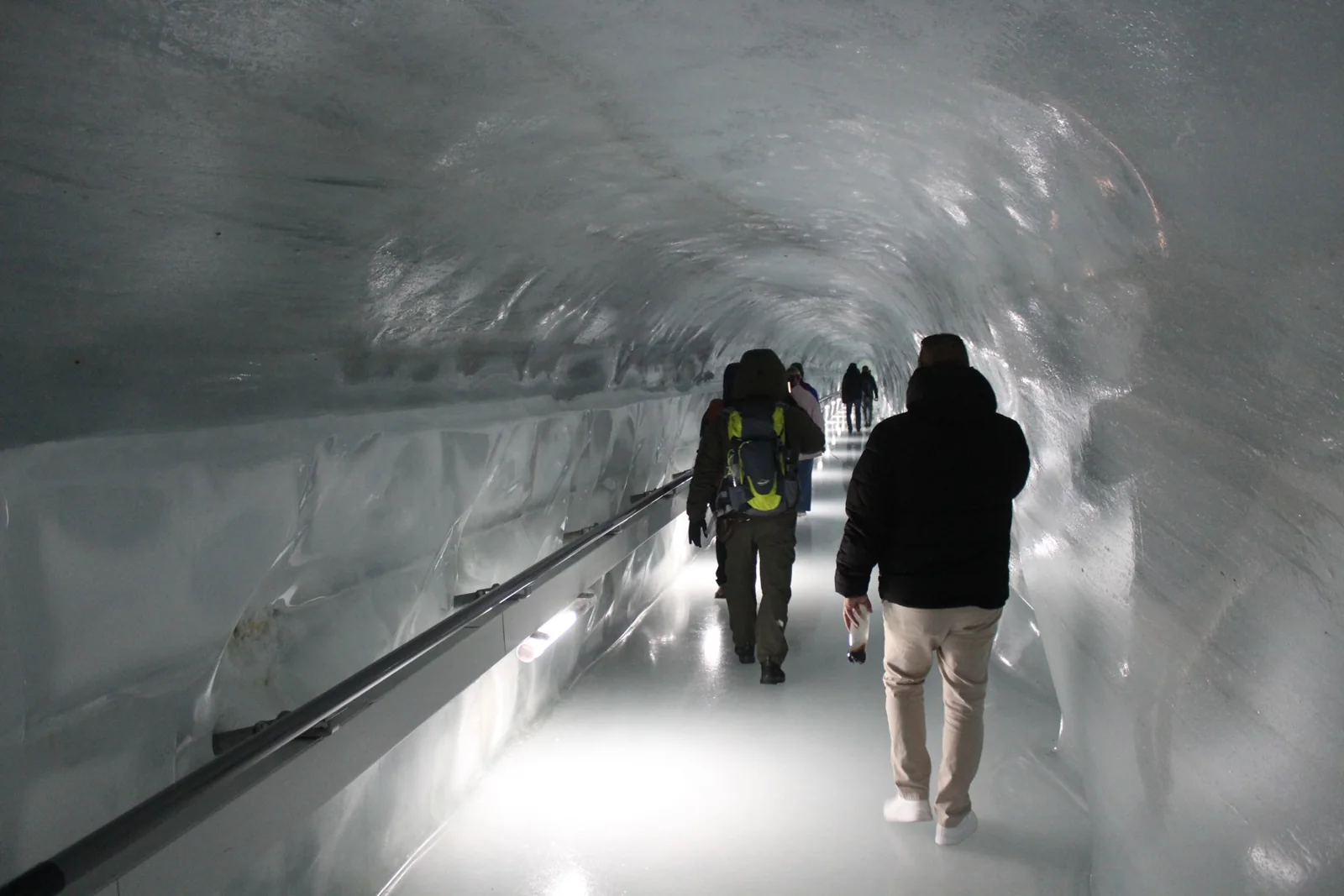 Visitantes de costas caminhando por um túnel iluminado do Palácio de Gelo