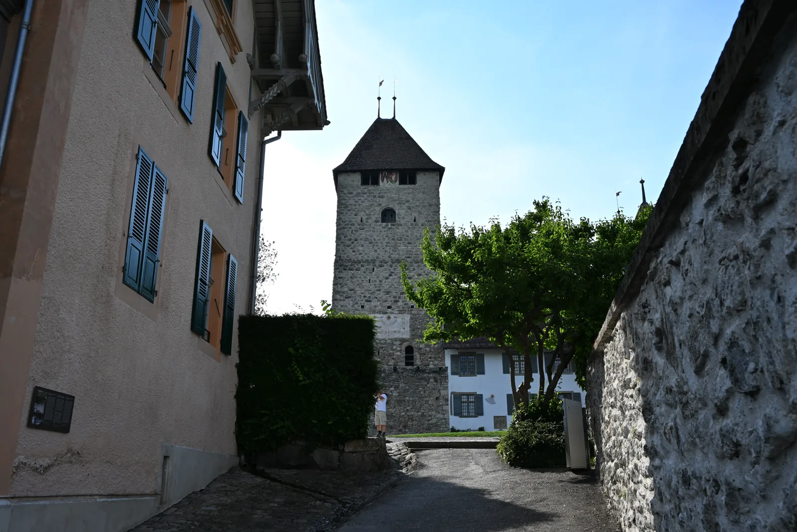 Caminho de pedra entre fachadas e muro, com a torre de Spiez ao fundo