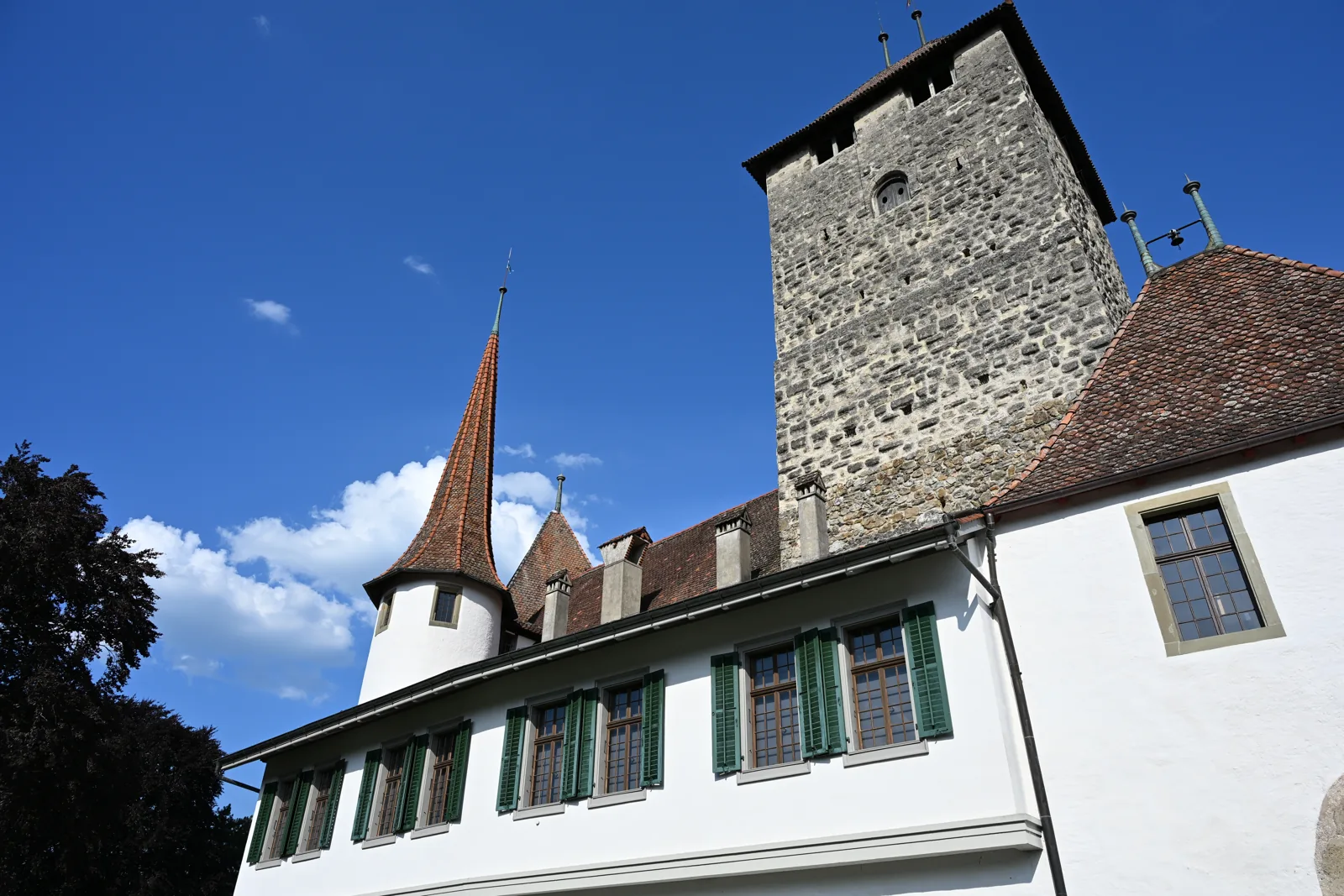 Torre de pedra do Castelo de Spiez acima da ala com persianas verdes